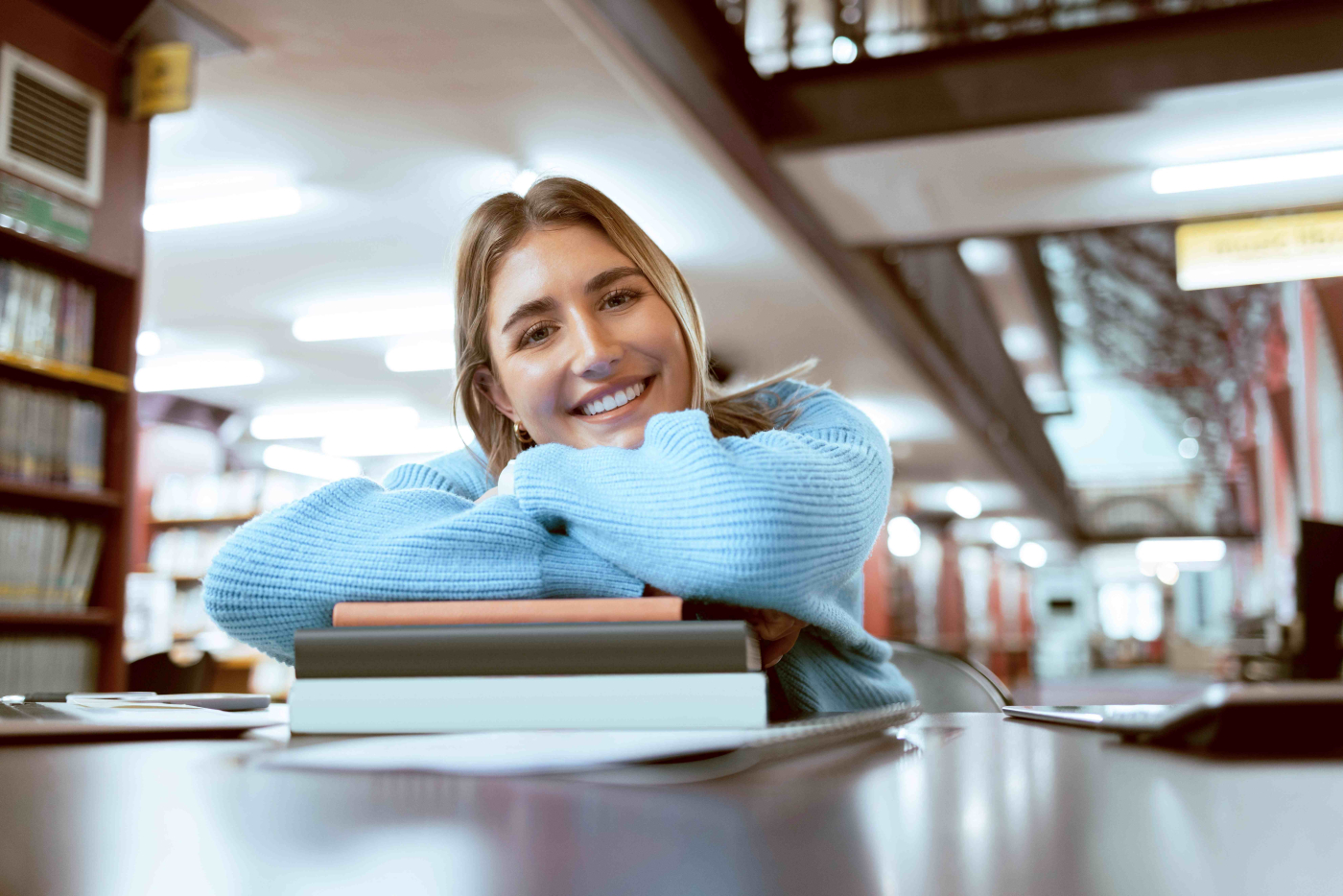 Junge Frau lehnt zufrieden über einem Stapel Bücher