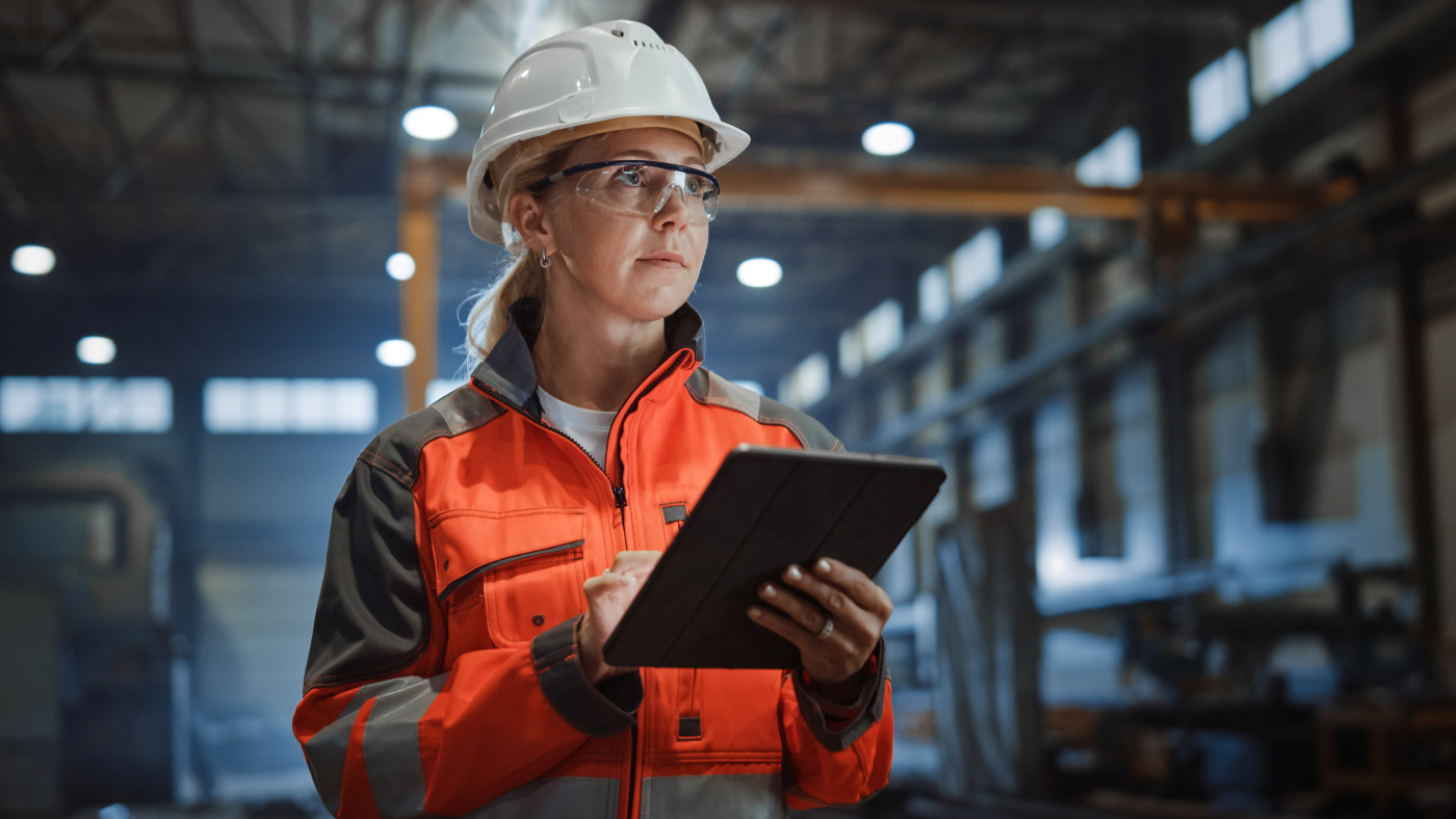 Junge Frau mit Bauhelm und Warnjacke, die am Tablet arbeitet